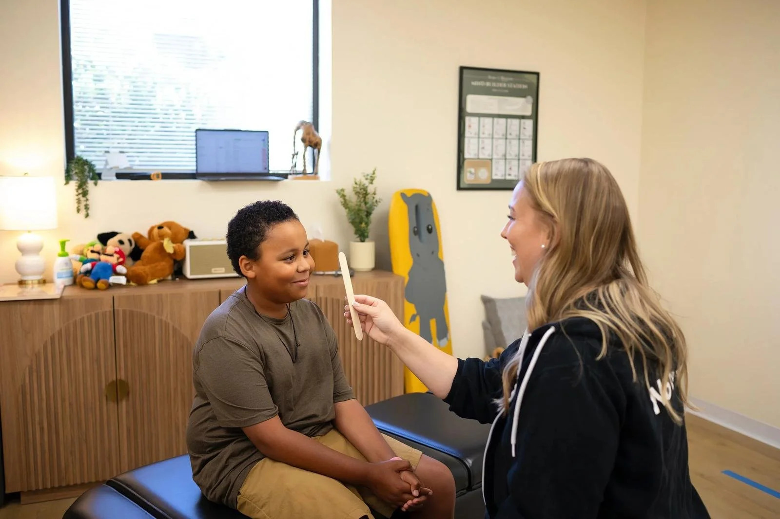 Dr. Jennifer Gordon sitting on a treatment table and holding a small item for a child seated across from her