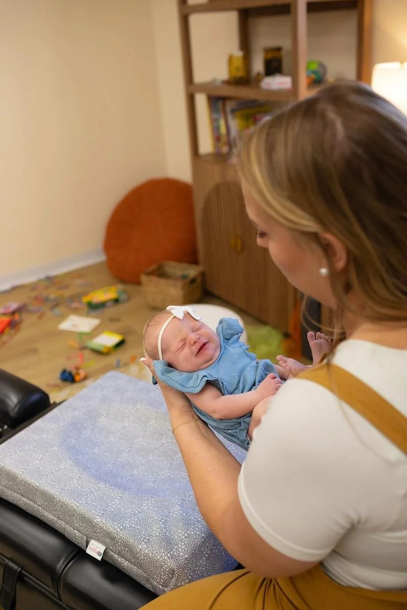 A chiropractor holding an infant above a padded treatment table